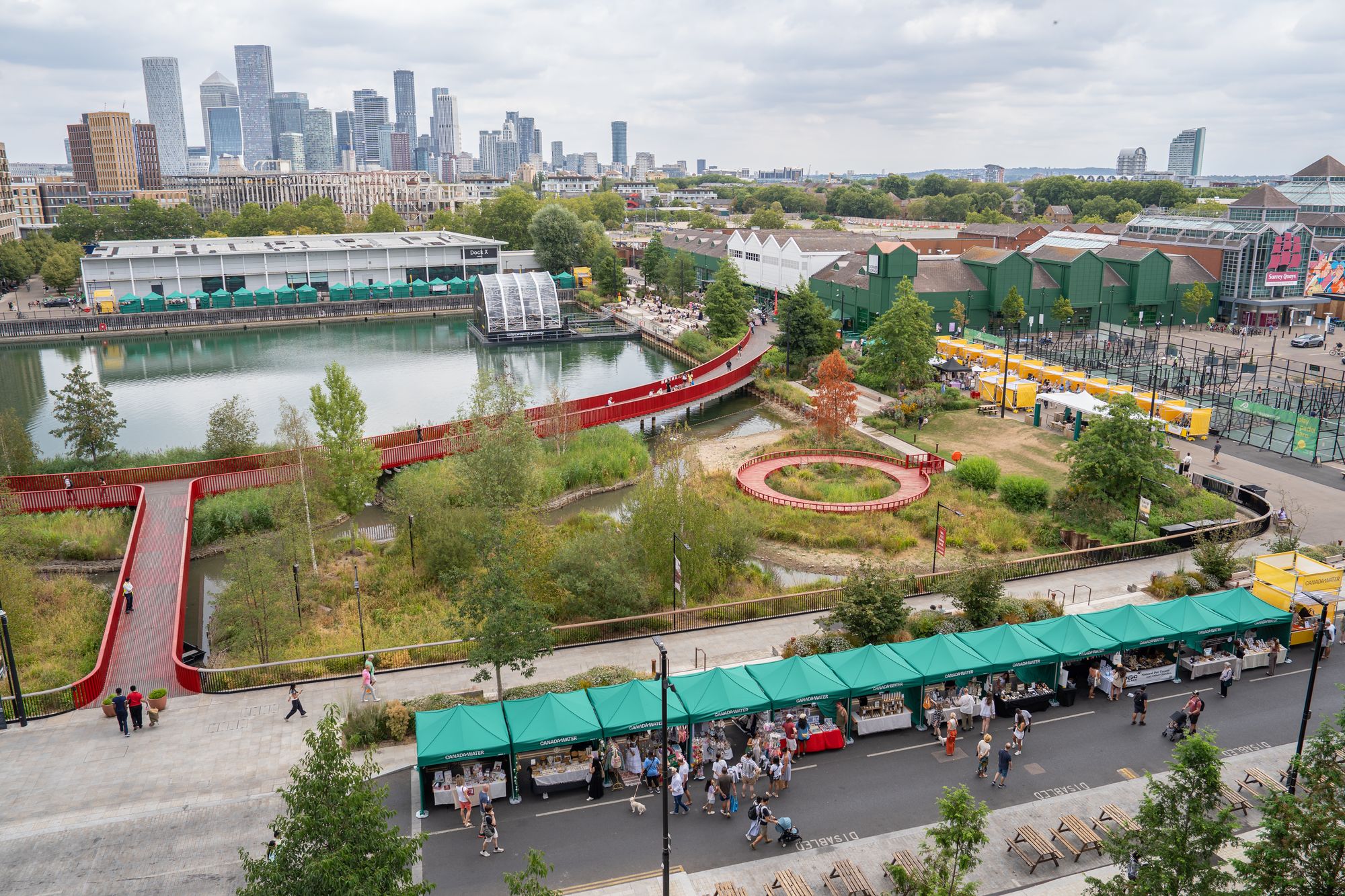 An elevated view of the Craft & Flea market stalls along Canada Dock, with the City of London skyline in the distance.