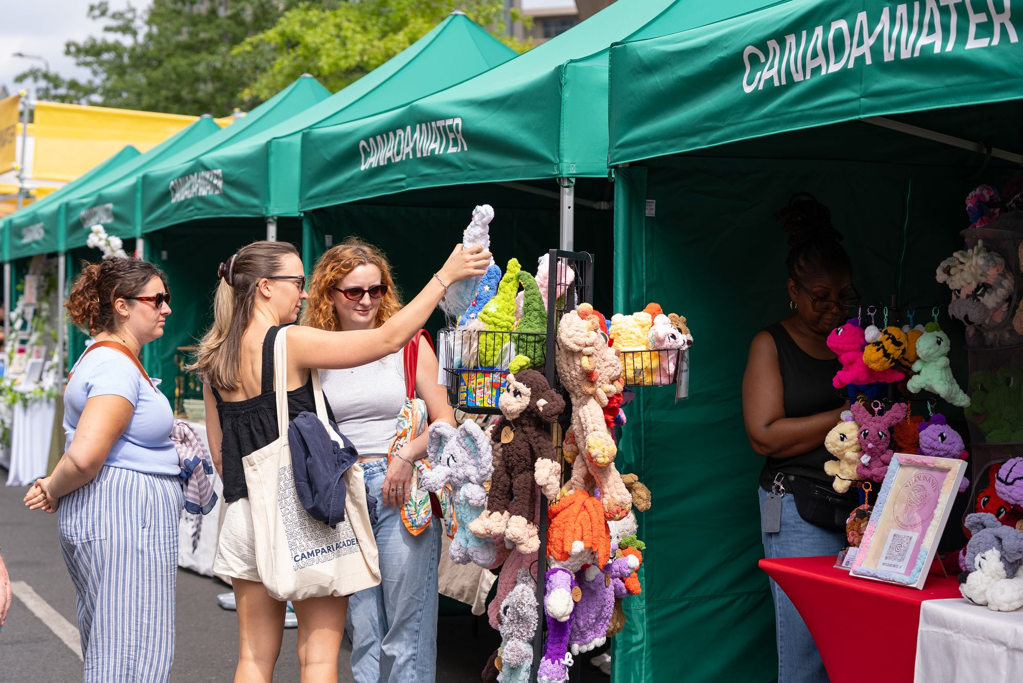 Friends browsing handmade gifts at a Craft & Flea market stall by Canada Dock.