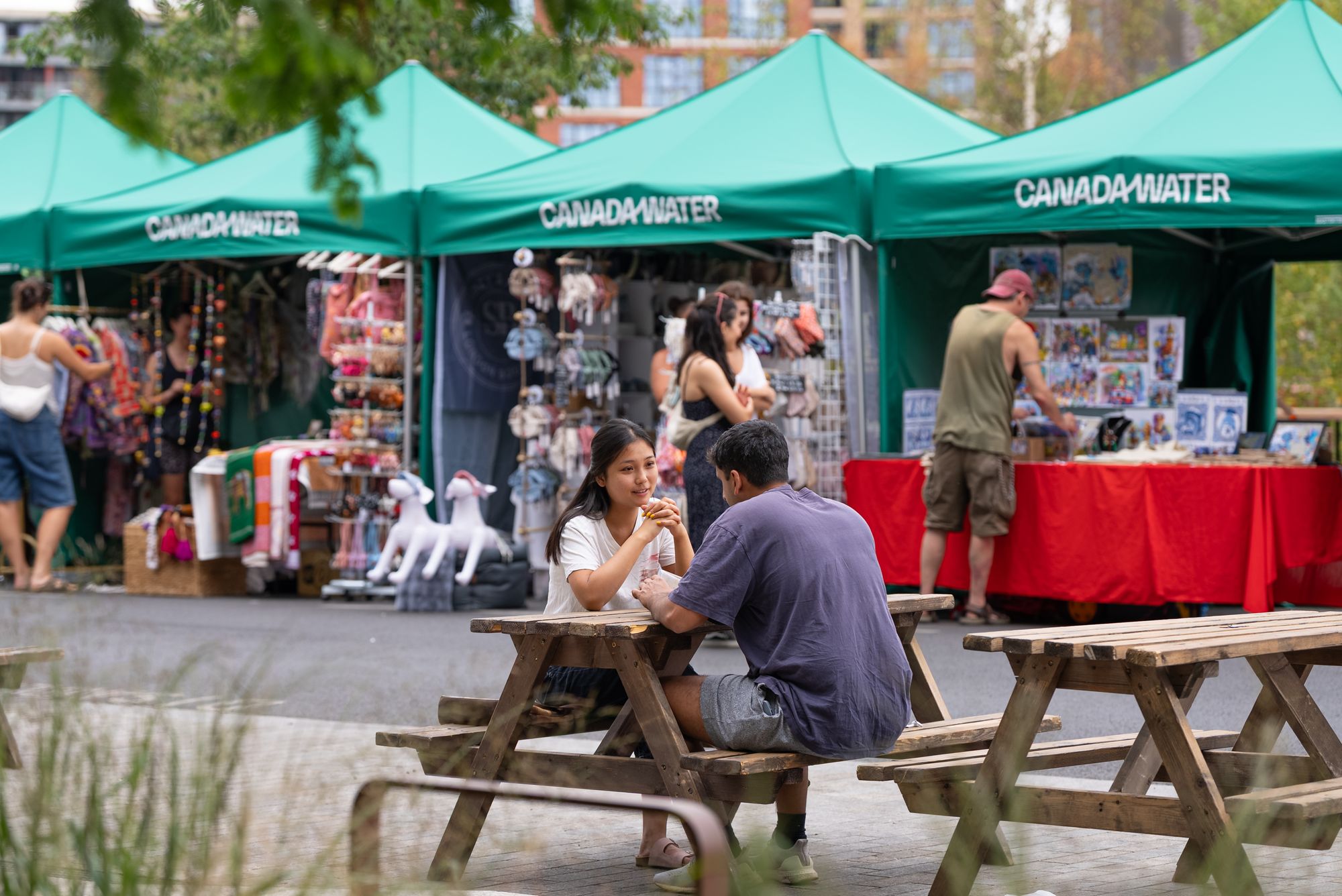Visitors at picnic benches between the Craft & Flea market stalls on the Canada Water dockside.