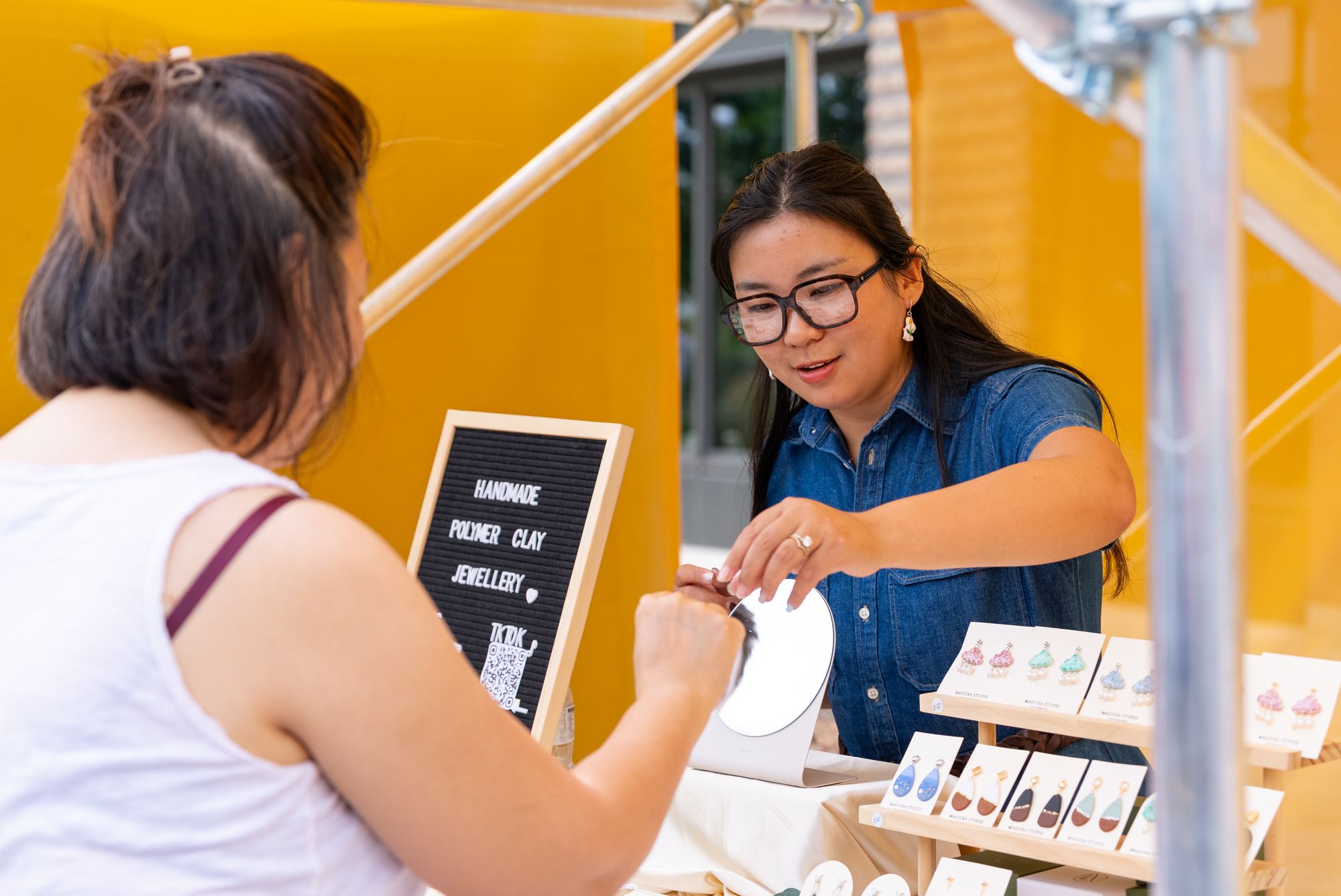 A trader showing her handmade jewellery to a customer at the Craft & Flea market, Canada Water.