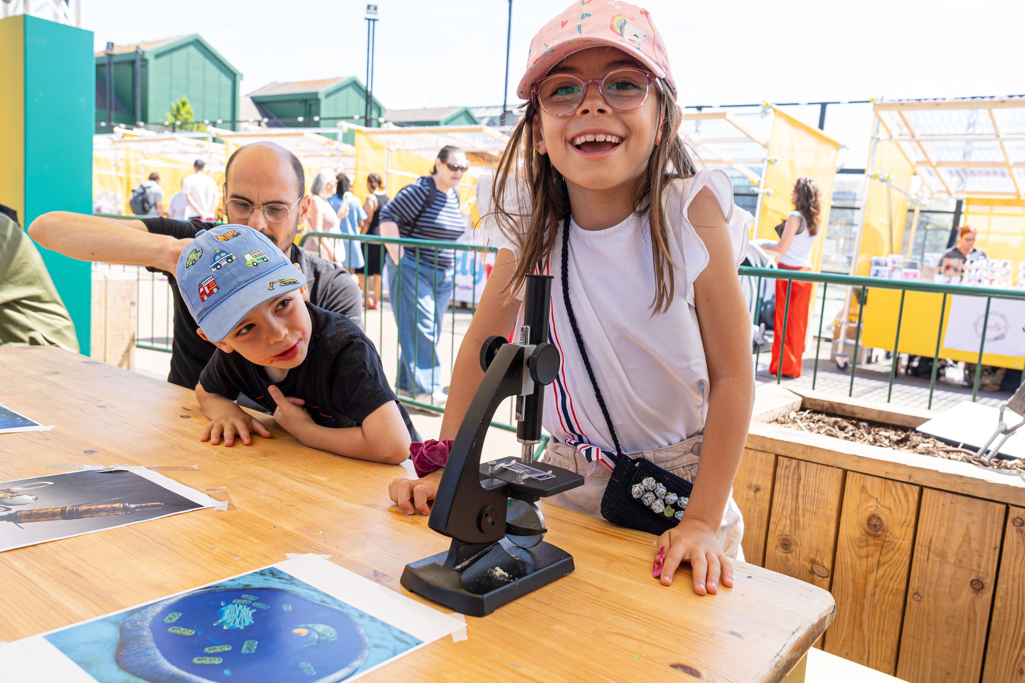 A child laughing at a microscope in the Dockside Den family zone at Round the Dock, Canada Water.