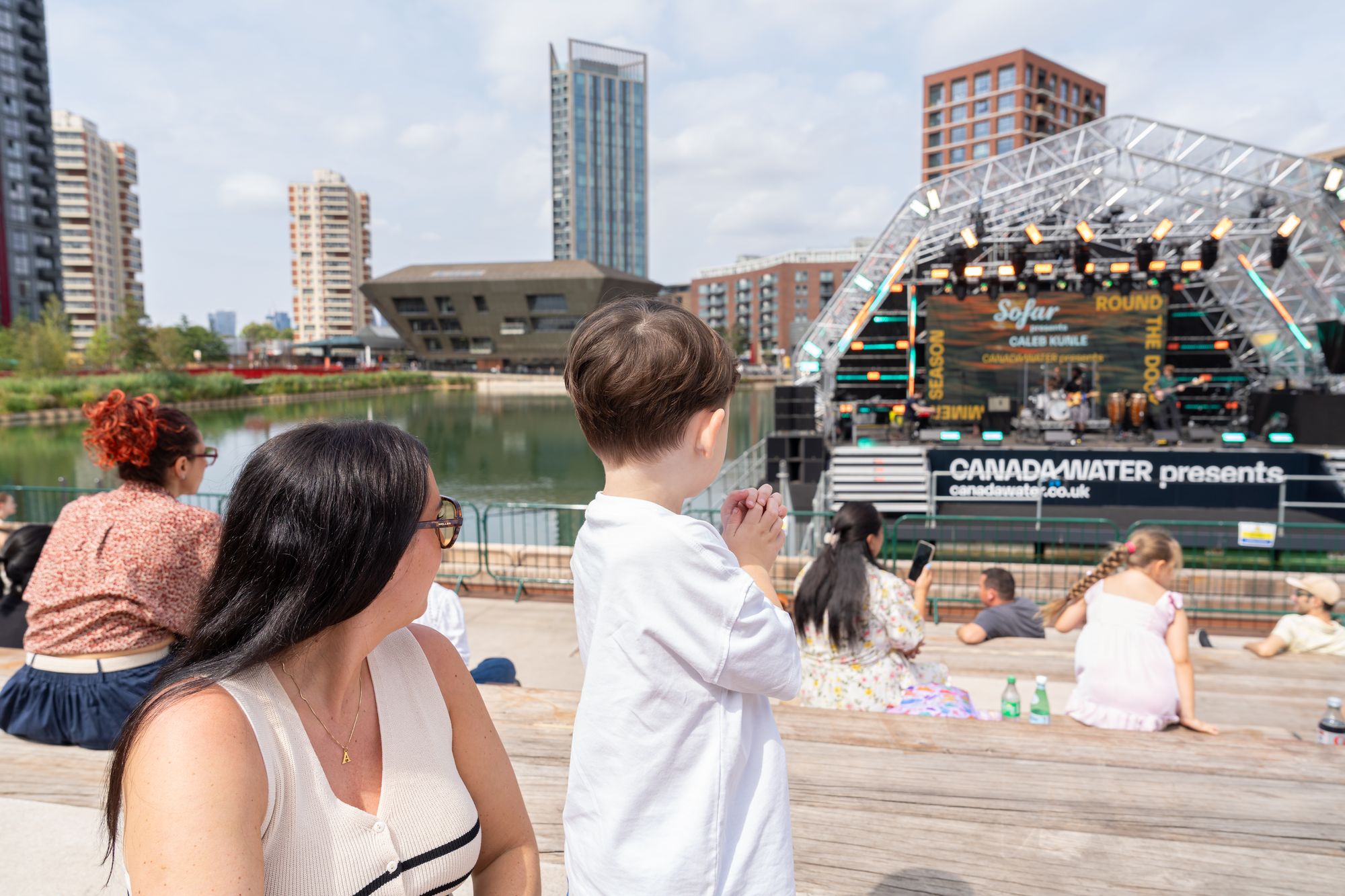 A family watching the floating stage from the dockside at Round the Dock, Canada Water.