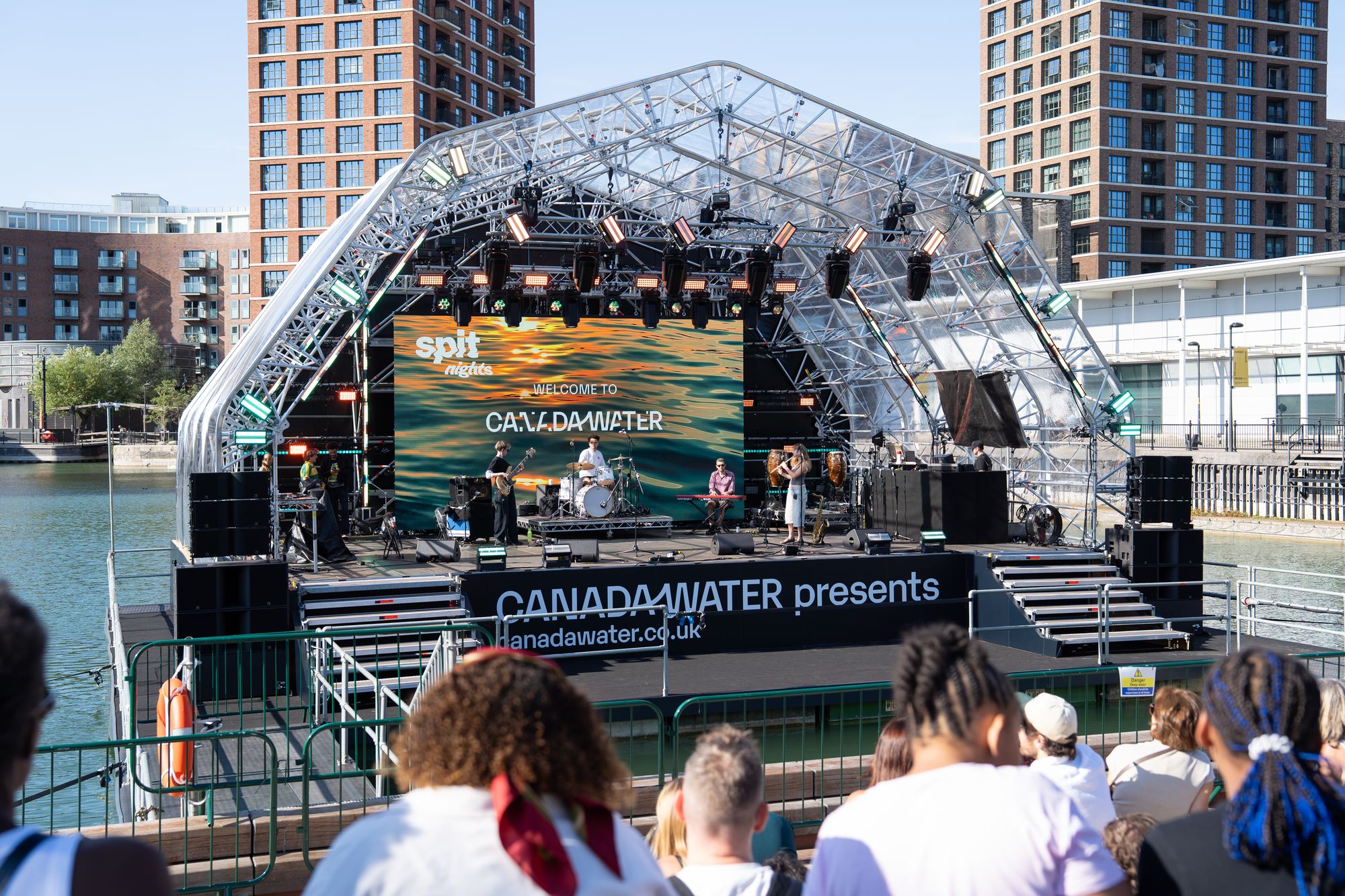 The Round the Dock floating stage on Canada Dock during Spit Night, with the audience on the water's edge.
