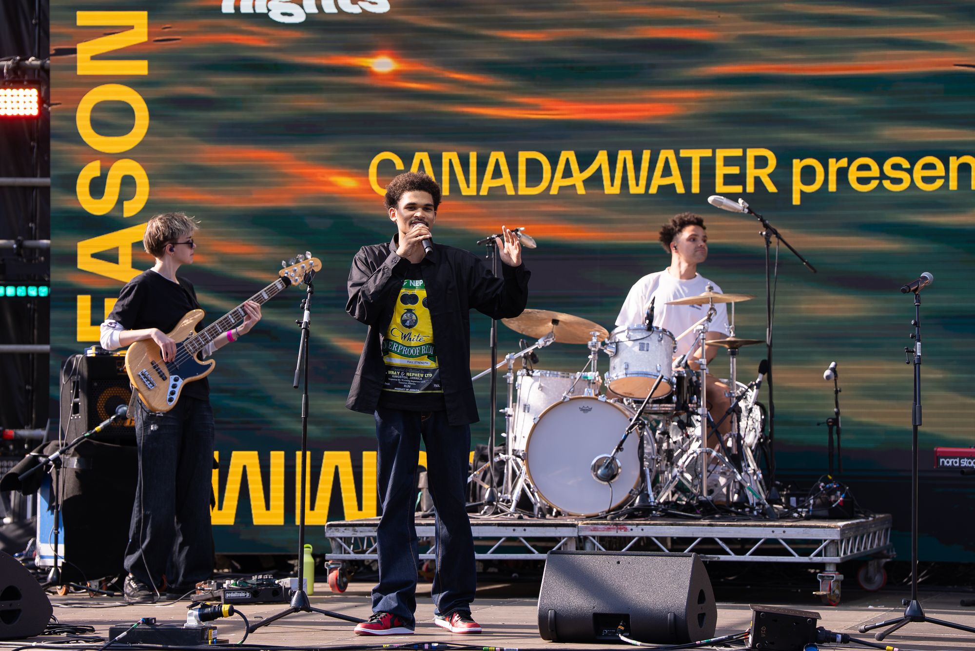 A poet performing with a live band in front of the Round the Dock screen at Spit Night, Canada Water.