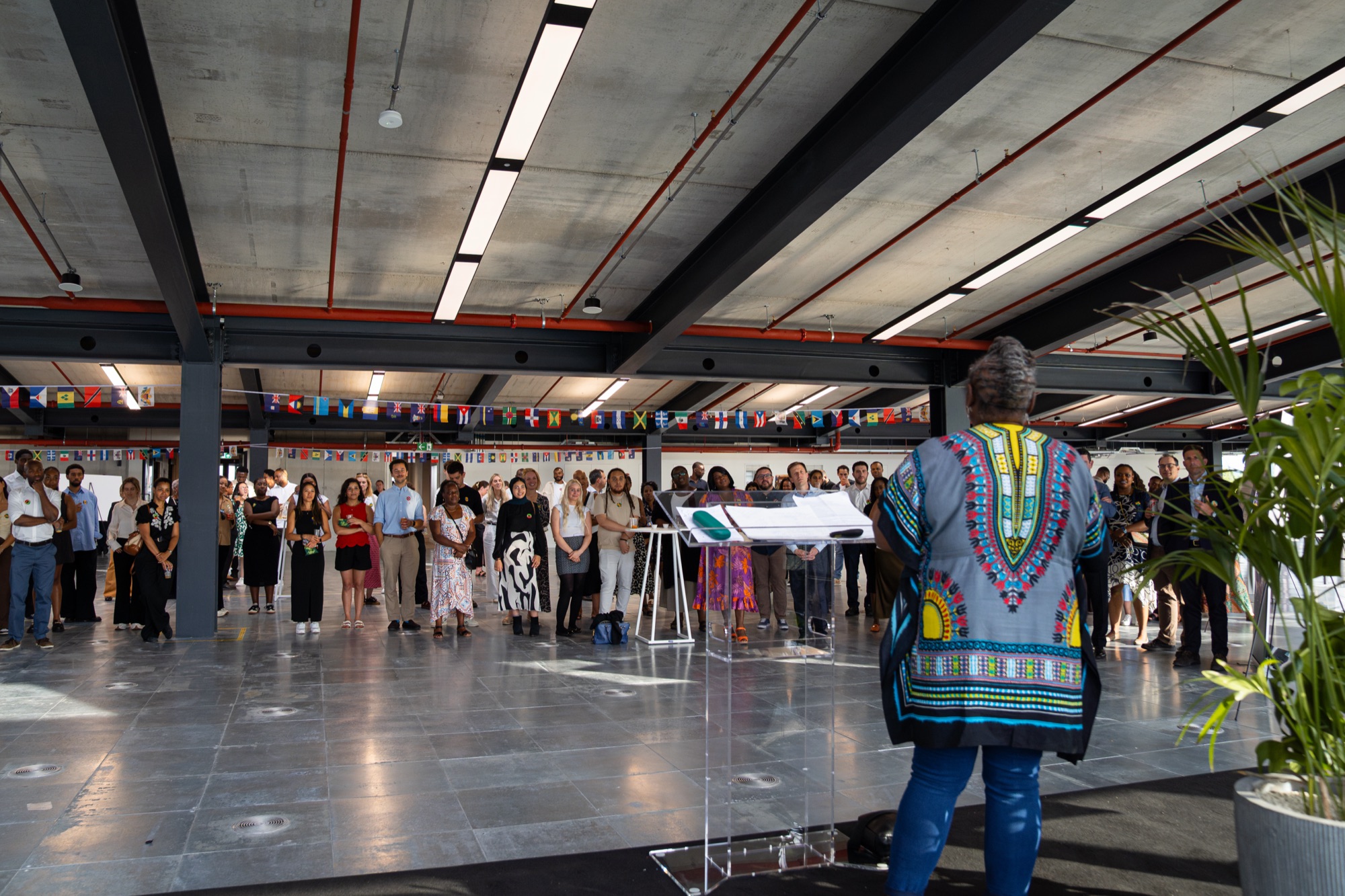 Dr Audrey Allwood addresses a full Dock Shed under Caribbean flag bunting at the Windrush celebration, Canada Water.