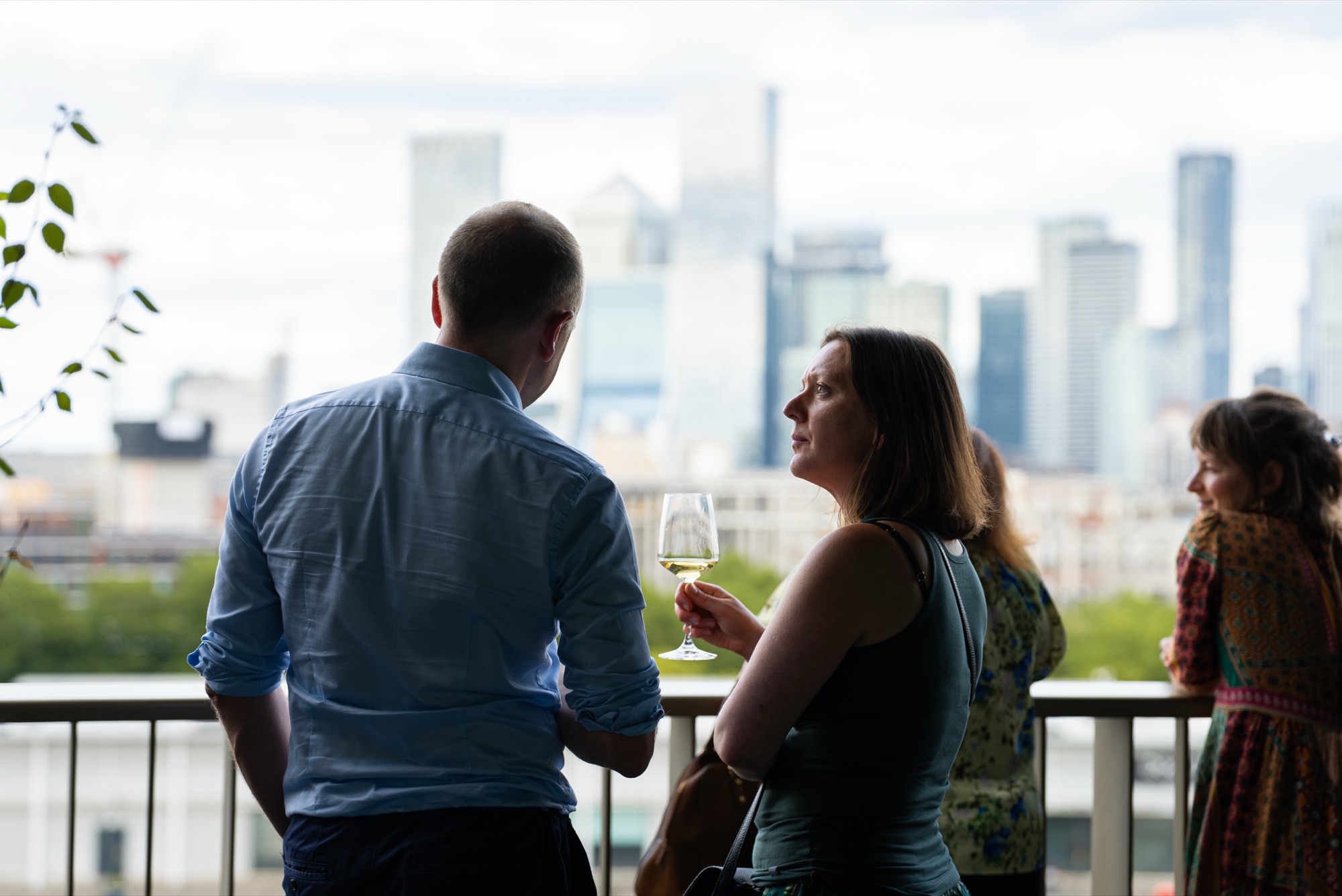 Guests networking with drinks on the Dock Shed balcony with the London skyline behind them at the Windrush celebration.