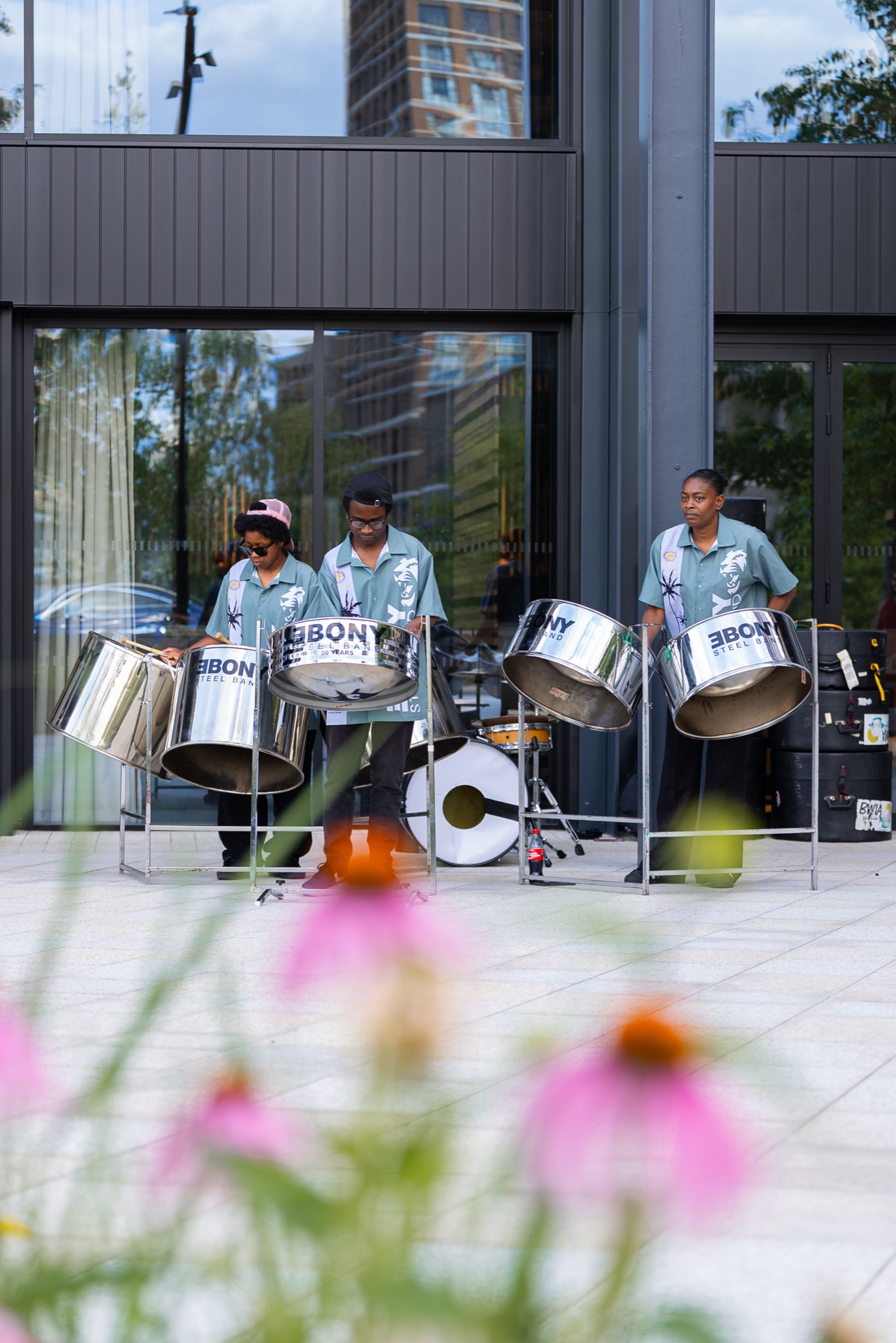 The steelpan band outside the Dock Shed seen through summer planting at Canada Water, London SE16.