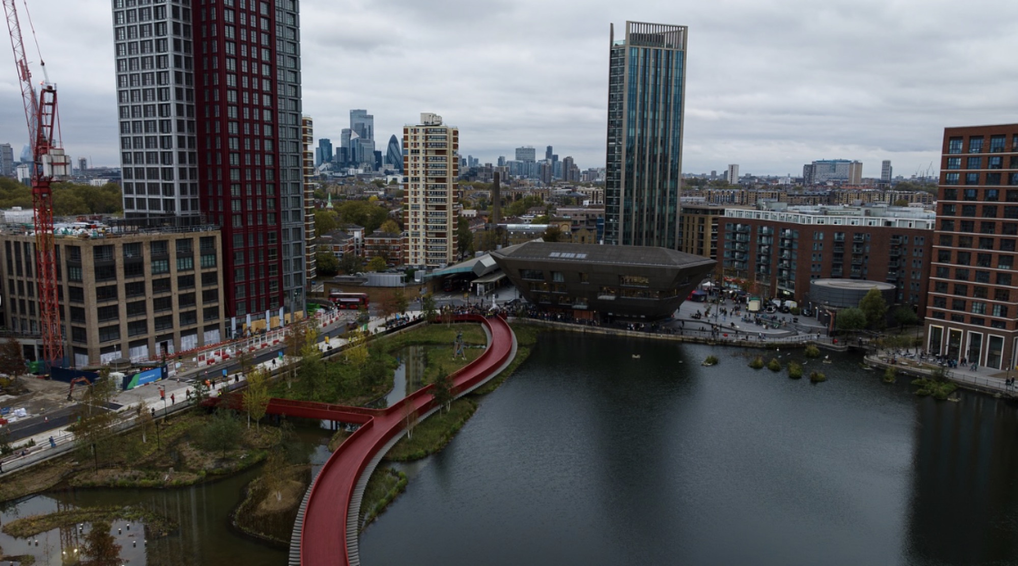 Drone shot showing the full length of the 170-metre red boardwalk spanning Canada Dock, with the London skyline beyond