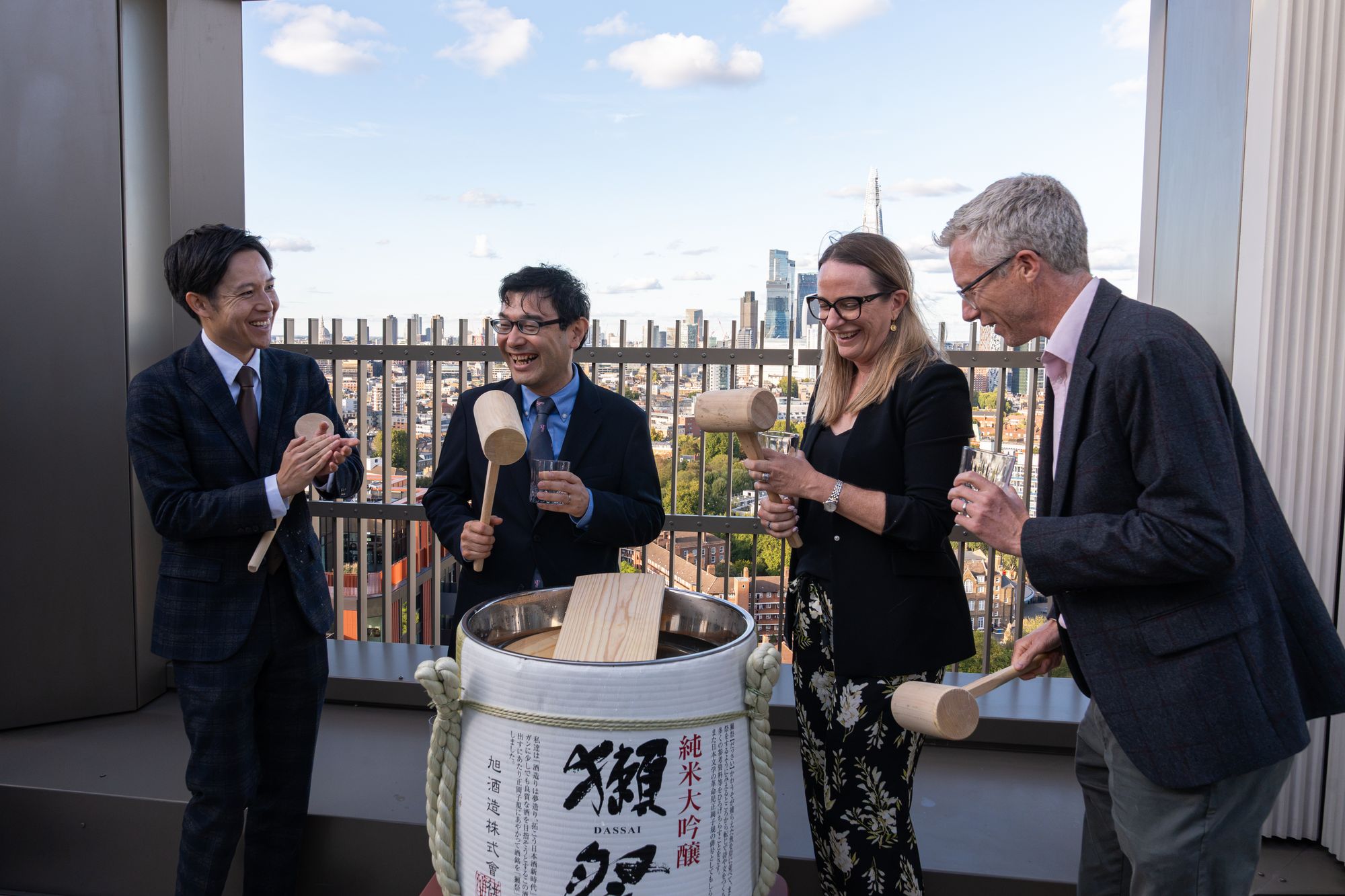 The Kagami Biraki sake barrel ceremony at the Arbour Heights launch — mallets raised on the roof terrace at The Wilderly, Elephant Park, with the City of London behind.