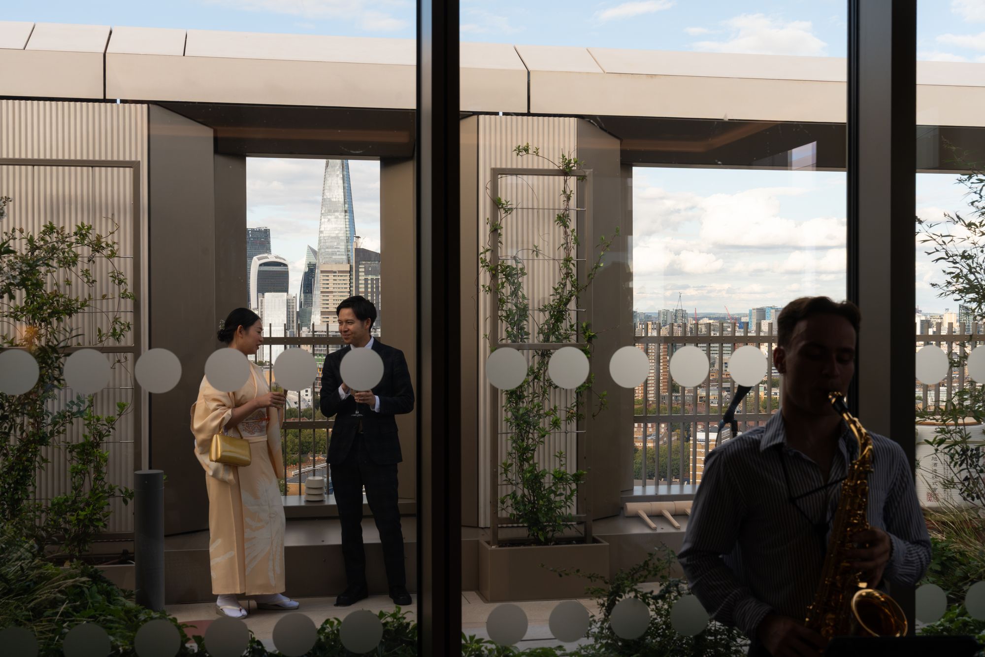 A guest in traditional kimono on the terrace as a saxophonist plays at the Arbour Heights launch, The Wilderly, London SE17.