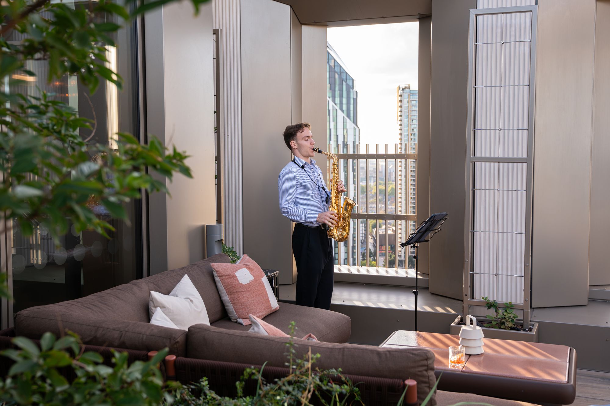 Saxophonist performing beside the terrace lounge seating at Arbour Heights — capturing the building's outdoor amenity space.
