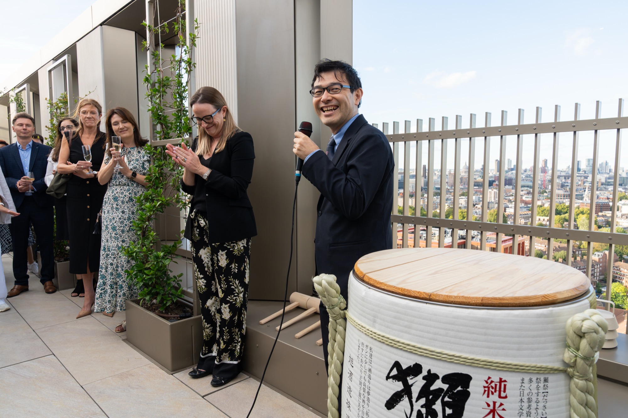 A host speaks beside the sake barrel on the Arbour Heights roof terrace — event photography for Lendlease at Elephant Park, London.