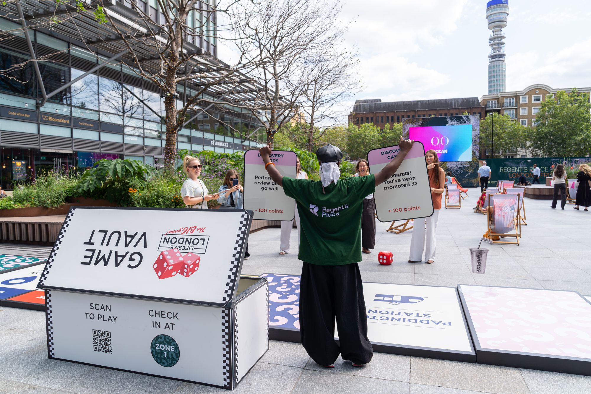 A costumed game host with Discovery Cards beside the Game Vault at Regent's Place, BT Tower in view.